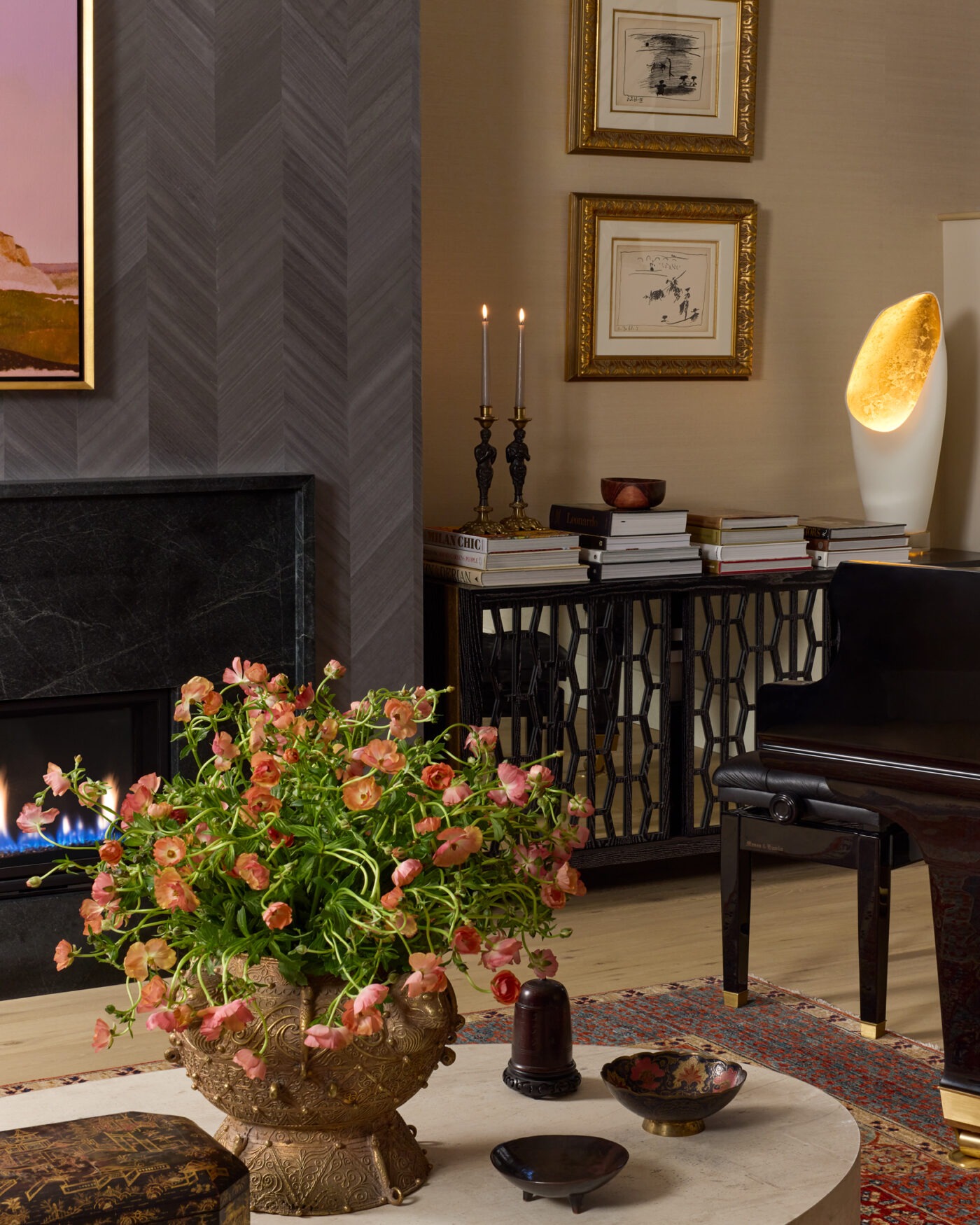 Rivington Marx Interiors Living room with a dark marble fireplace, chevron wallcovering, grand piano, and pink floral arrangement.